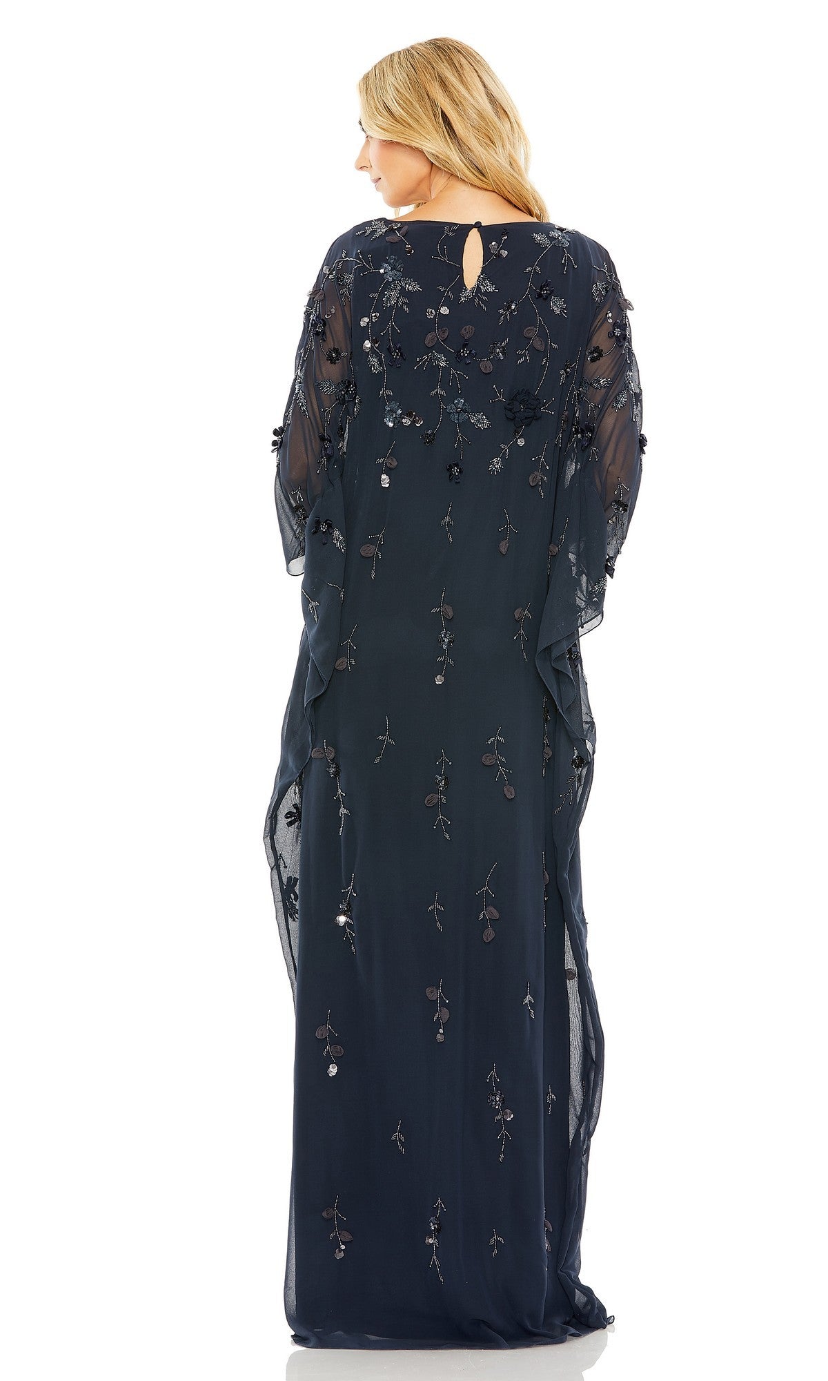 A woman with blonde hair stands facing away, wearing the Mac Duggal 9242 Trapeze Embellished Formal Gown in sheer navy blue with delicate floral embroidery and a small back keyhole opening.